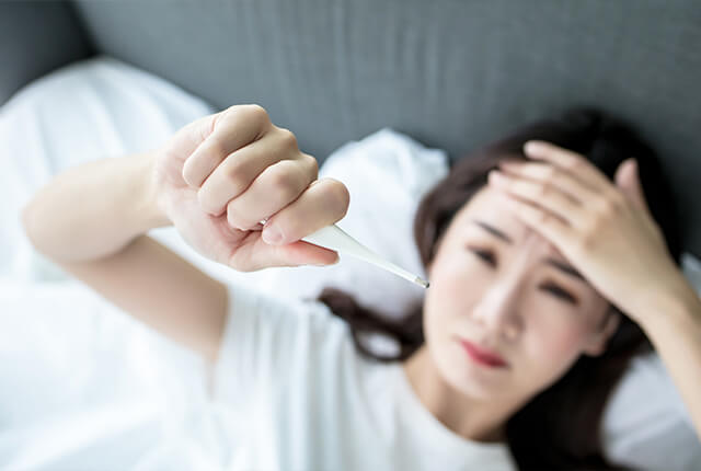 ベッドに横になりながら体温計を見ている女性